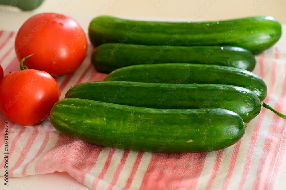 Fresh cucumbers and ripe tomatoes arranged on a striped kitchen towel in morning light Fresh cucumbers and ripe tomatoes arranged on a striped kitchen towel in morning light