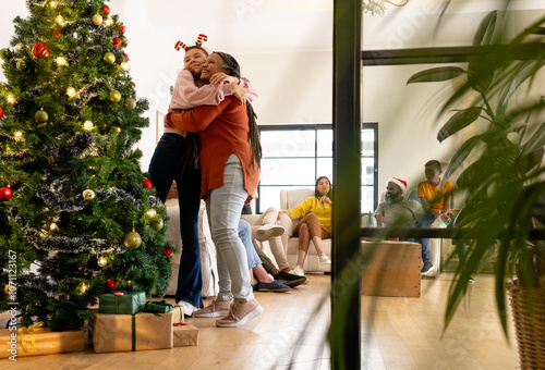 multiracial family celebrating Christmas at home, hugging near decorated tree, feeling joyful photo