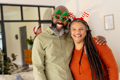Happy multiracial couple wearing festive accessories, smiling together at home during Christmas