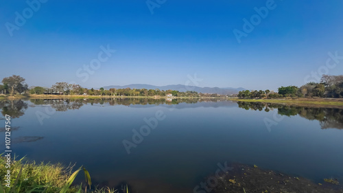 A panoramic view of Nong Bua Lake in Chiang Rai, Thailand, showcasing its serene waters surrounded by lush greenery and distant mountains. 