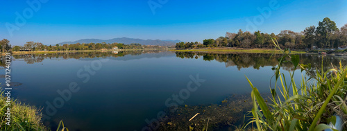 A panoramic view of Nong Bua Lake in Chiang Rai, Thailand, showcasing its serene waters surrounded by lush greenery and distant mountains. 