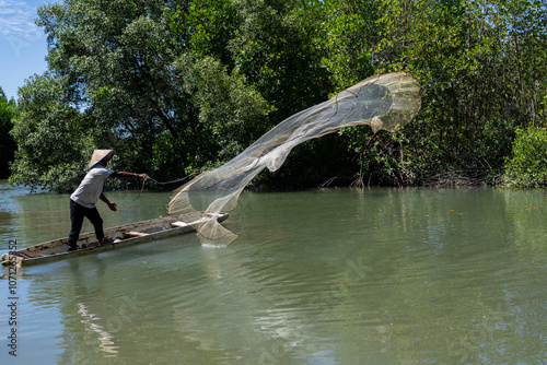 A fisherman throwing a fishing net from a boat in a mangrove forest near the coast