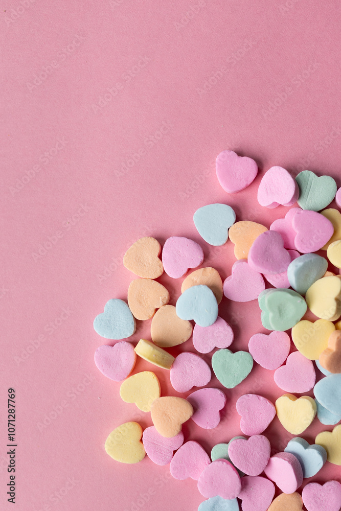 flat lay of a pile of pastel colored candy hearts in blue, green, pink, yellow, and orange against a pink background with copy space available, valentine's day themed flat lay of a pile of pastel colored candy hearts in blue, green, pink, yellow, and orange against a pink background with copy space available, valentine's day themed