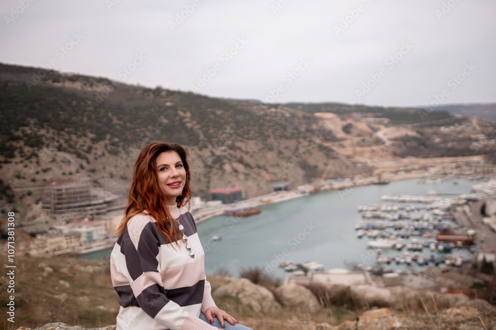 A woman is sitting on a rock overlooking a body of water. The scene is peaceful and serene, with the woman looking out over the water and taking in the view. A woman is sitting on a rock overlooking a body of water. The scene is peaceful and serene, with the woman looking out over the water and taking in the view.