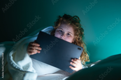 Canvas Print Kid lying on bed and surfing Internet on tablet in dark room