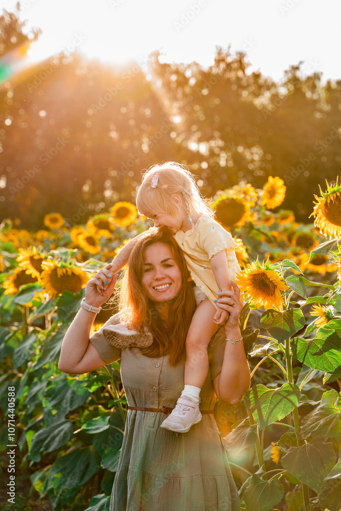  Mother holding little child girl daughter and  having fun in the field of sunflowers in summer. Summer season, freedom, family value concept.