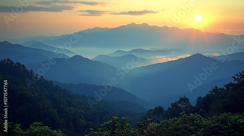 A breathtaking sunrise over a mountain range, the sun peeking through the clouds, casting a warm glow over the landscape. The mountains are layered in the distance, with fog filling the valleys.