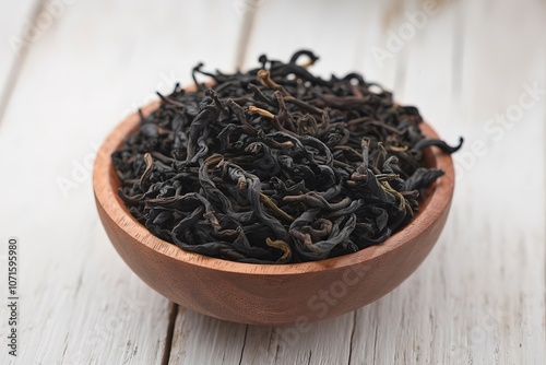 A photo of a wooden bowl filled with black, dried tea leaves photo