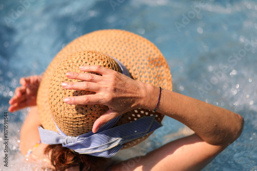 Tableau sur toile straw hat with a woman's hand relaxing in a luxury resort pool water