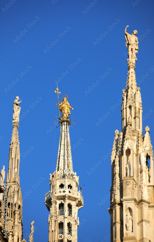 golden statue of Virgin Mary and blue sky in background in Milan Cathedral in Italy golden statue of Virgin Mary and blue sky in background in Milan Cathedral in Italy