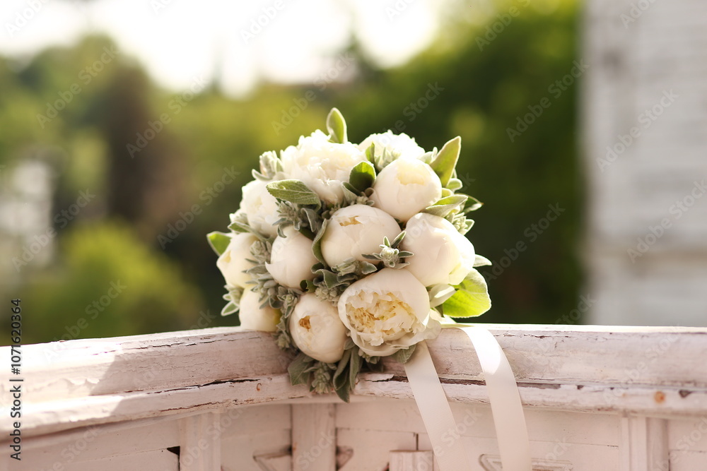 Simple and elegant white peony wedding bouquet with greenery, resting on a rustic wooden railing