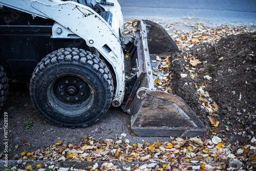 The modern skid steer small excavator working with soil on construction site. Close up. Autumn