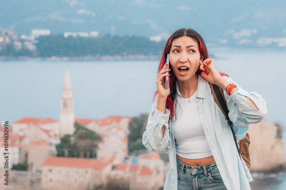 A woman struggles with poor phone reception while talking in front of Adriatic coastal resort town, reflecting challenges in mobile connectivity for travelers.