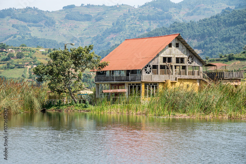 A solitary tree stands in a serene lake with mountains behind, Uganda