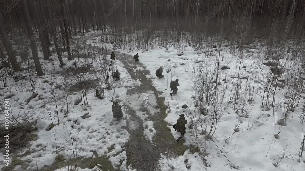 AERIAL VIEW: Group of fully equipped soldiers in camouflage uniform armed with assault rifles, machine gun moving on abandoned path along dense forest at winter during reconnaissance military mission