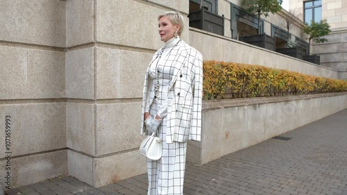 Fashionable Mature Woman with Short Hair Standing Outside in City Dressed in Stylish Checkered White Suit with Blazer, Accessories and Handbag Showcasing Trendy Clothing and Street Style