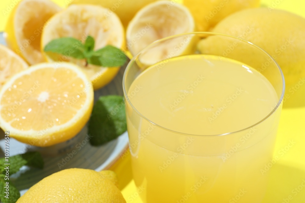 Glass of fresh lemon juice and squeezed fruits on yellow background, closeup Glass of fresh lemon juice and squeezed fruits on yellow background, closeup