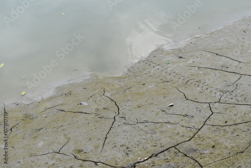 A close-up of dried river soil, showing deep cracks and a rough, textured surface. The parched ground reflects the effects of drought and water scarcity