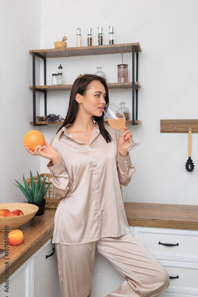 Young woman in loungewear enjoying a fresh start to her day with a glass of juice and a grapefruit. Relaxed, modern kitchen atmosphere promoting wellness, healthy living, and self-care. Young woman in loungewear enjoying a fresh start to her day with a glass of juice and a grapefruit. Relaxed, modern kitchen atmosphere promoting wellness, healthy living, and self-care.