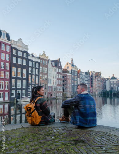 Two friends sit by the peaceful canal, admiring the charming autumn colors of Amsterdam historic buildings. The warm atmosphere invites exploration and connection during this picturesque season. photo