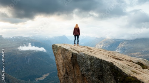 A person stands on a cliff overlooking expansive, scenic mountains beneath a dramatic sky, evoking the thrill of exploration and awe in nature's beauty.