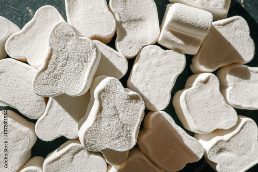 A close-up of fluffy, textured white marshmallows shaped like bones, arranged haphazardly under soft natural lighting. Shadows create depth, highlighting their unique surface details A close-up of fluffy, textured white marshmallows shaped like bones, arranged haphazardly under soft natural lighting. Shadows create depth, highlighting their unique surface details