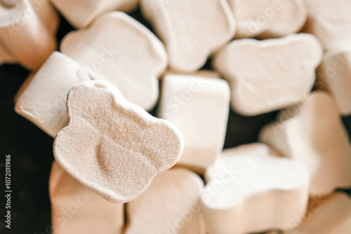 A close-up of fluffy, textured white marshmallows shaped like bones, arranged haphazardly under soft natural lighting. Shadows create depth, highlighting their unique surface details photo