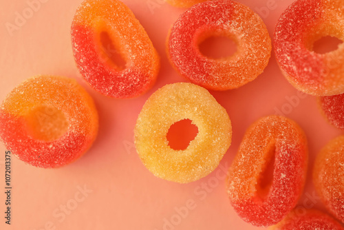 Quadro su tela Close-up of sugar-coated gummy candy rings in vibrant red, orange, and yellow tones placed on a soft peach-colored background