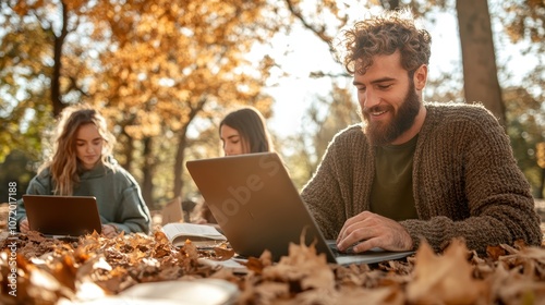 A group of friends happily work on laptops outdoors, surrounded by fallen autumn leaves, symbolizing teamwork, collaboration, and enjoying the beauty of nature together. photo