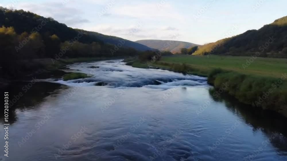 A picturesque river with gentle rapids, flowing through a quiet countryside with rolling hills in the background A picturesque river with gentle rapids, flowing through a quiet countryside with rolling hills in the background