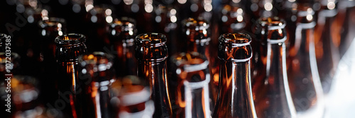 Header image of dozen open glass bottles shining in light at production line in craft beer factory, copy space photo