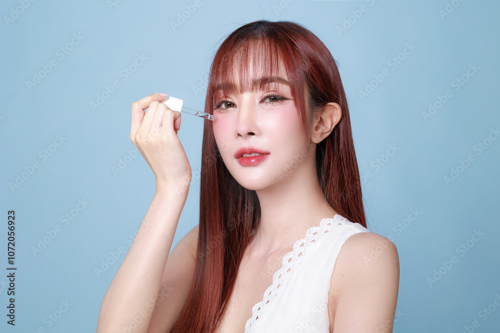 Obraz premium Beautiful young Asian woman model long hair using dropper bottle to apply serum on face clean fresh skin on isolated blue background. Cute girl portrait, Facial treatment, Body care, Beauty and Spa.
