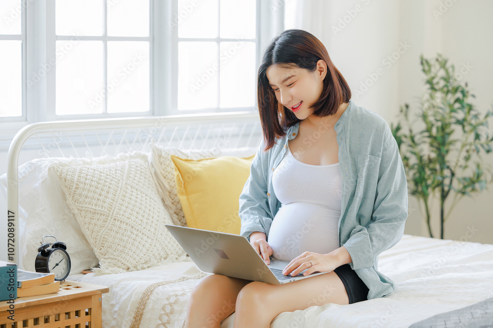 Young Asian happy pregnant woman is sitting and relaxing on bed and touching her belly. Family plan, pregnancy, motherhood, people and expectation concept Young Asian happy pregnant woman is sitting and relaxing on bed and touching her belly. Family plan, pregnancy, motherhood, people and expectation concept