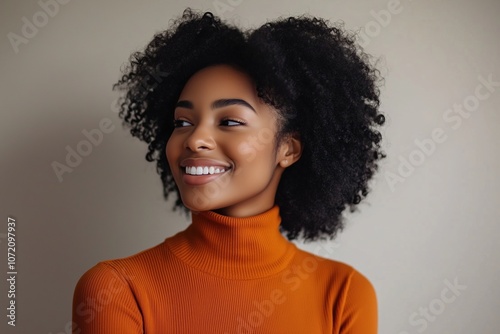 A woman with curly hair is smiling and wearing an orange sweater