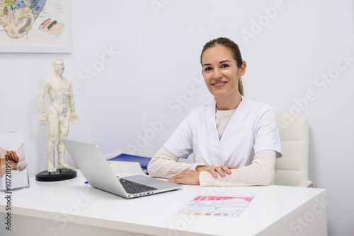 Doctor working at her desk in acupuncture office smiling at camera photo