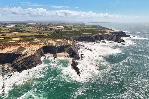 Bird's eye view of the rocky ocean shoreline and lighthouse Cabo Sardao in the distance, Portugal