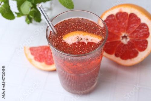 Glass of drink with chia seeds and grapefruit on white tiled table, closeup