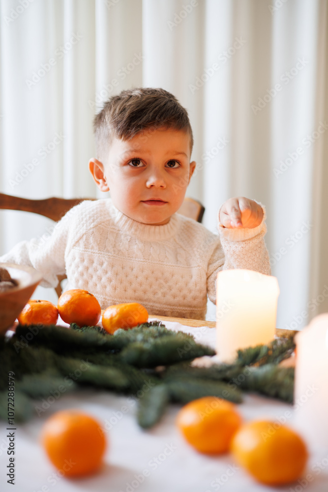 Toddler boy pointing at candle on Christmas dinning table with tangerines and spruce branches at home Toddler boy pointing at candle on Christmas dinning table with tangerines and spruce branches at home