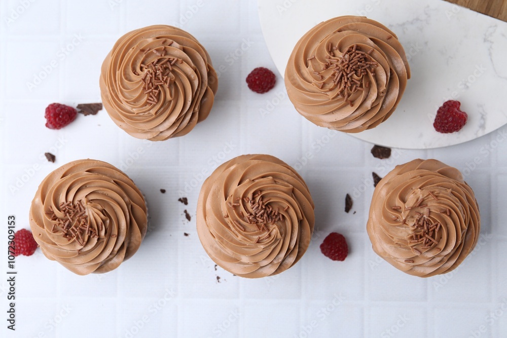 Tasty cupcakes with chocolate cream and raspberries on white tiled table, flat lay Tasty cupcakes with chocolate cream and raspberries on white tiled table, flat lay