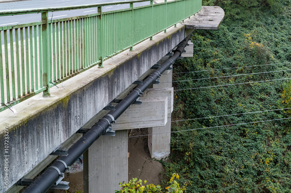 Large black pipes running under concrete bridge with green railing Large black pipes running under concrete bridge with green railing