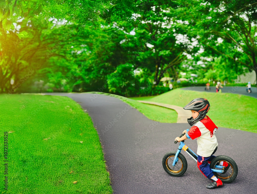 4 years old boy in safety helmeriding balance bike at summer park green trees enjoy happy childhood. .Kids on bicycle in sunny park. Sport for kids.