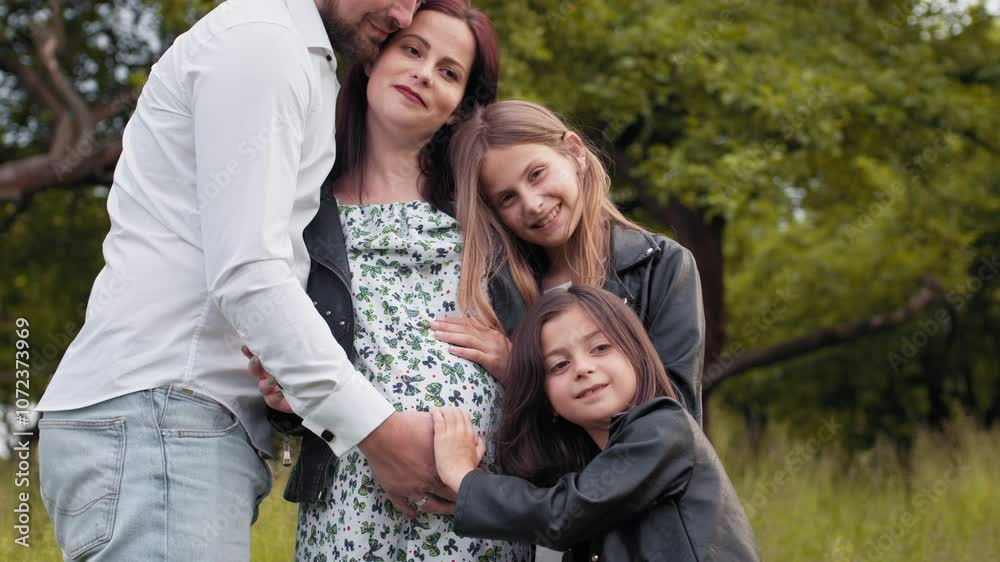 Caucasian family of four standing in strong hugs at green summer garden. Father, mother and two daughters spending weekends on fresh air. Caucasian family of four hugging at green summer garden. Caucasian family of four standing in strong hugs at green summer garden. Father, mother and two daughters spending weekends on fresh air. Caucasian family of four hugging at green summer garden.