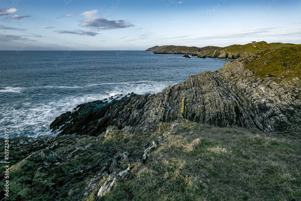 A rocky coastline stretches out into a vast blue ocean. The sky is clear and blue, with a few white clouds scattered across it. The sea is calm and the waves are gentle. A rocky coastline stretches out into a vast blue ocean. The sky is clear and blue, with a few white clouds scattered across it. The sea is calm and the waves are gentle.