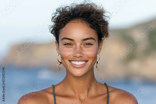 A woman smiling openly with distinct earrings stands in front of a calming sea backdrop, embodying joy and relaxation in a sea-inspired setting.