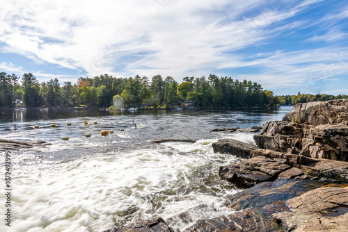 Bala Falls cascades into the Moon River, Ontario, showcasing a stunning natural landscape surrounded by lush forests and serene waters.