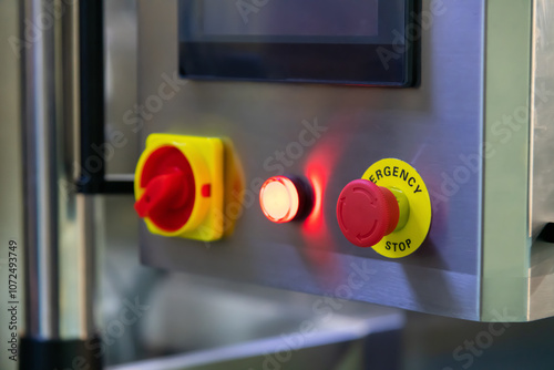 Close-up view of red Emergency Stop button on metal control panel of manufacturing machine in modern industrial building. Soft focus. Safety and security on workplace theme.