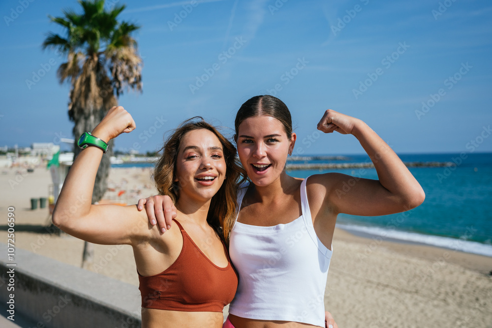 Two fit women showing their biceps on the beach embracing female empowerment Two fit women showing their biceps on the beach embracing female empowerment