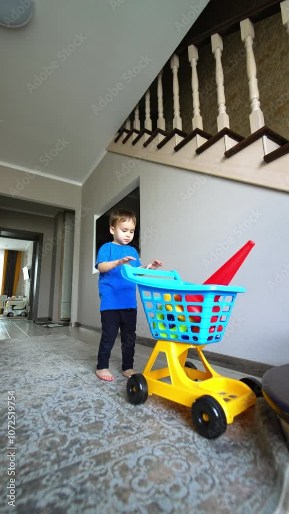 Toddler kid picked his toys in a trolley. Baby boy leaves the room pushing his cart. Low angle view. Vertical video. Toddler kid picked his toys in a trolley. Baby boy leaves the room pushing his cart. Low angle view. Vertical video.