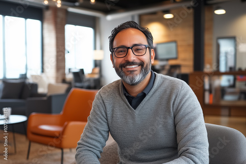 A friendly man with glasses enjoys his time in a contemporary workspace filled with stylish furniture