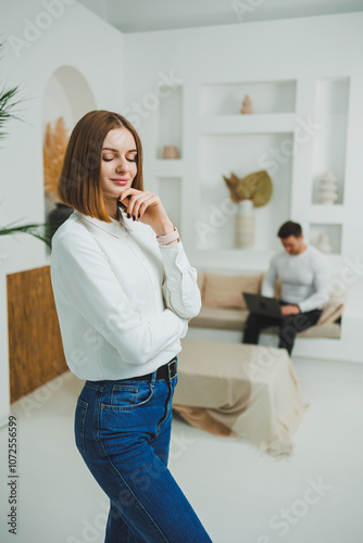 A cute woman is standing in a bright room at home. Woman in casual clothes relaxing at home.